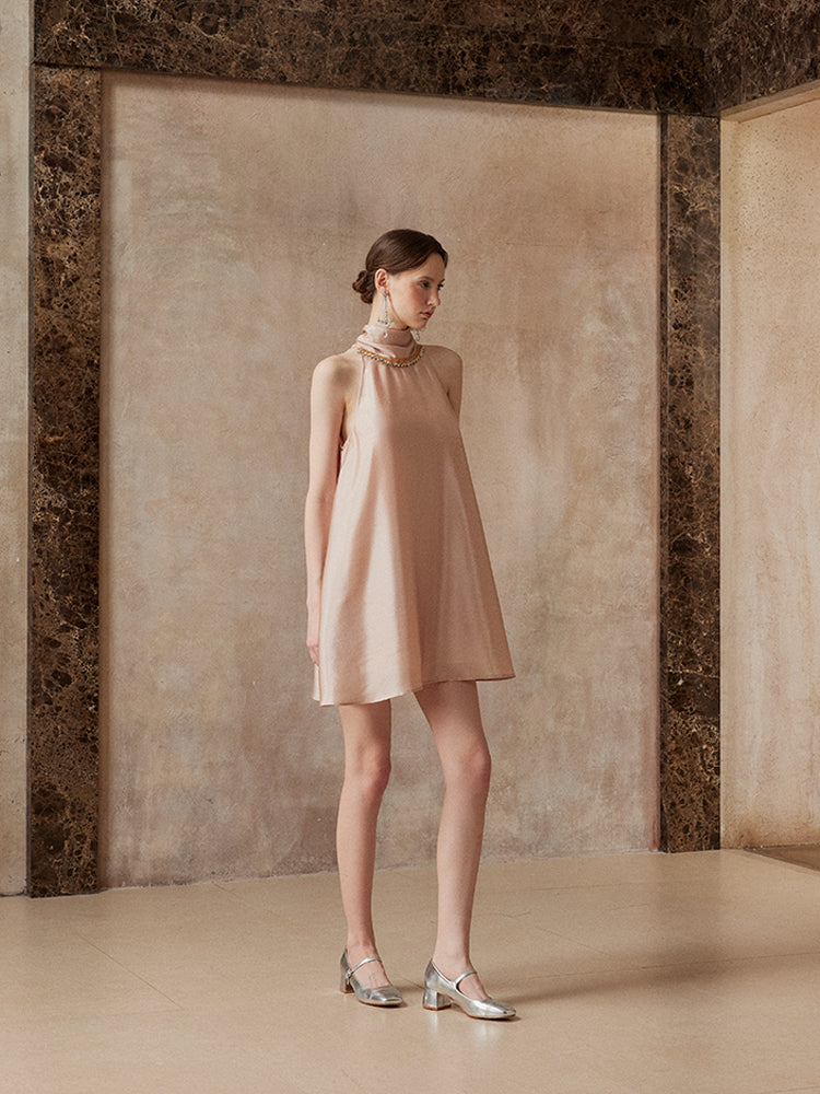 Woman wearing a beige dress standing against a textured wall.
