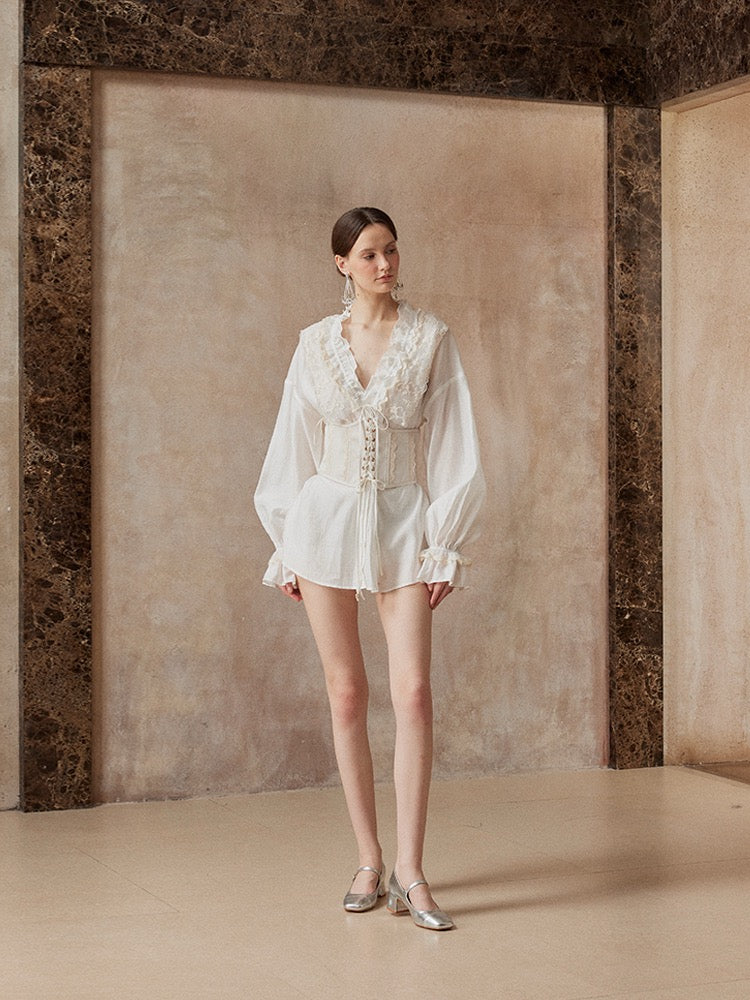 Woman wearing a white outfit standing against a textured wall.