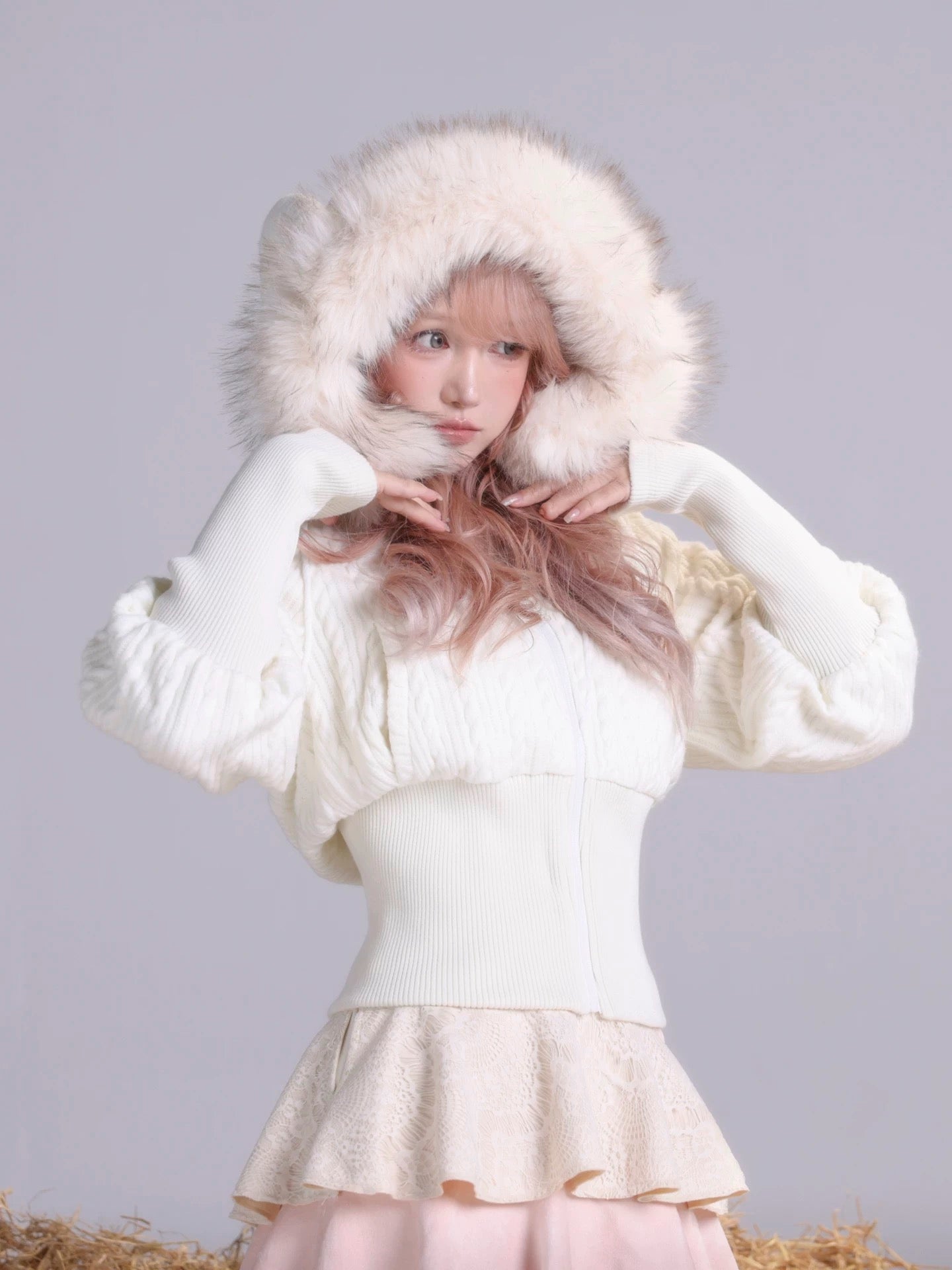 Girl wearing a white faux fur coat with sheep ears on hood on a gray background