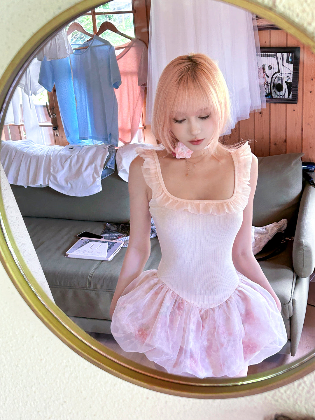 Woman in pink hair wearing a pastel pink ballet dress with floral pattern outfit in front of a mirror.