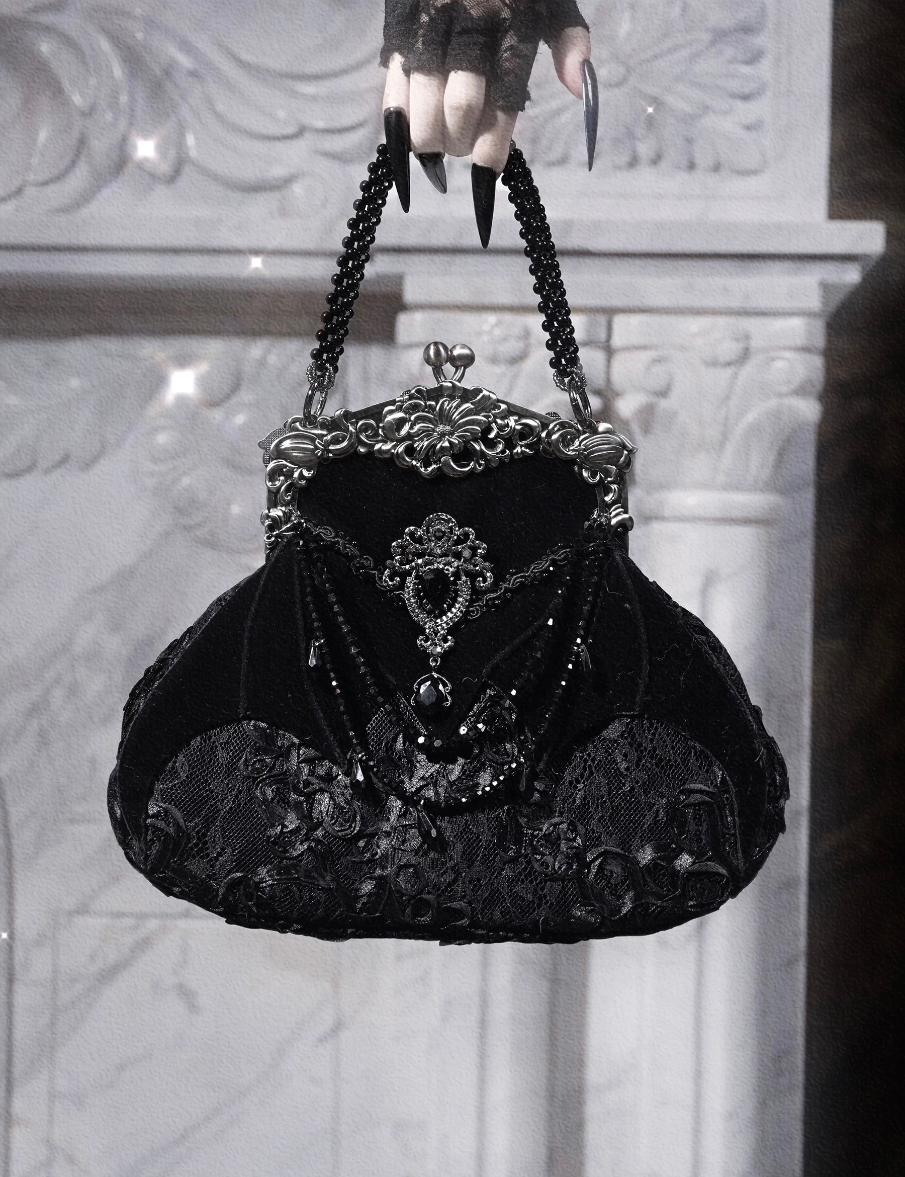 Black velvet handbag with intricate detailing held by a gloved hand against a textured white background