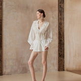 Woman in a white outfit standing against a textured wall.
