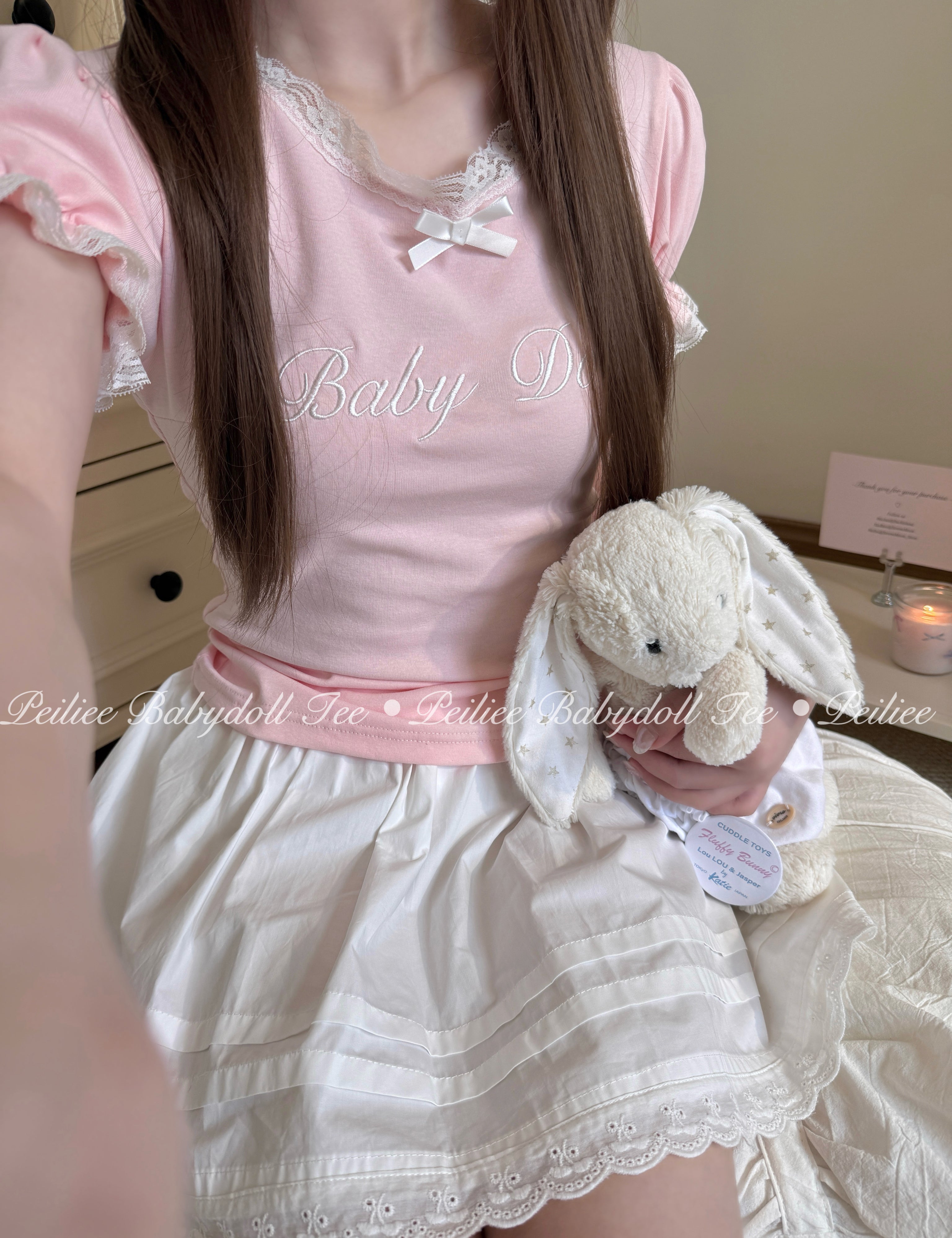 Girl wearing a pink peiliee design cottonn babydoll top and white skirt holding a plush bunny.