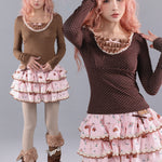 Two women wearing matching polka pot print sweatshirt with brown tops and pink ruffled skirts on a plain background.