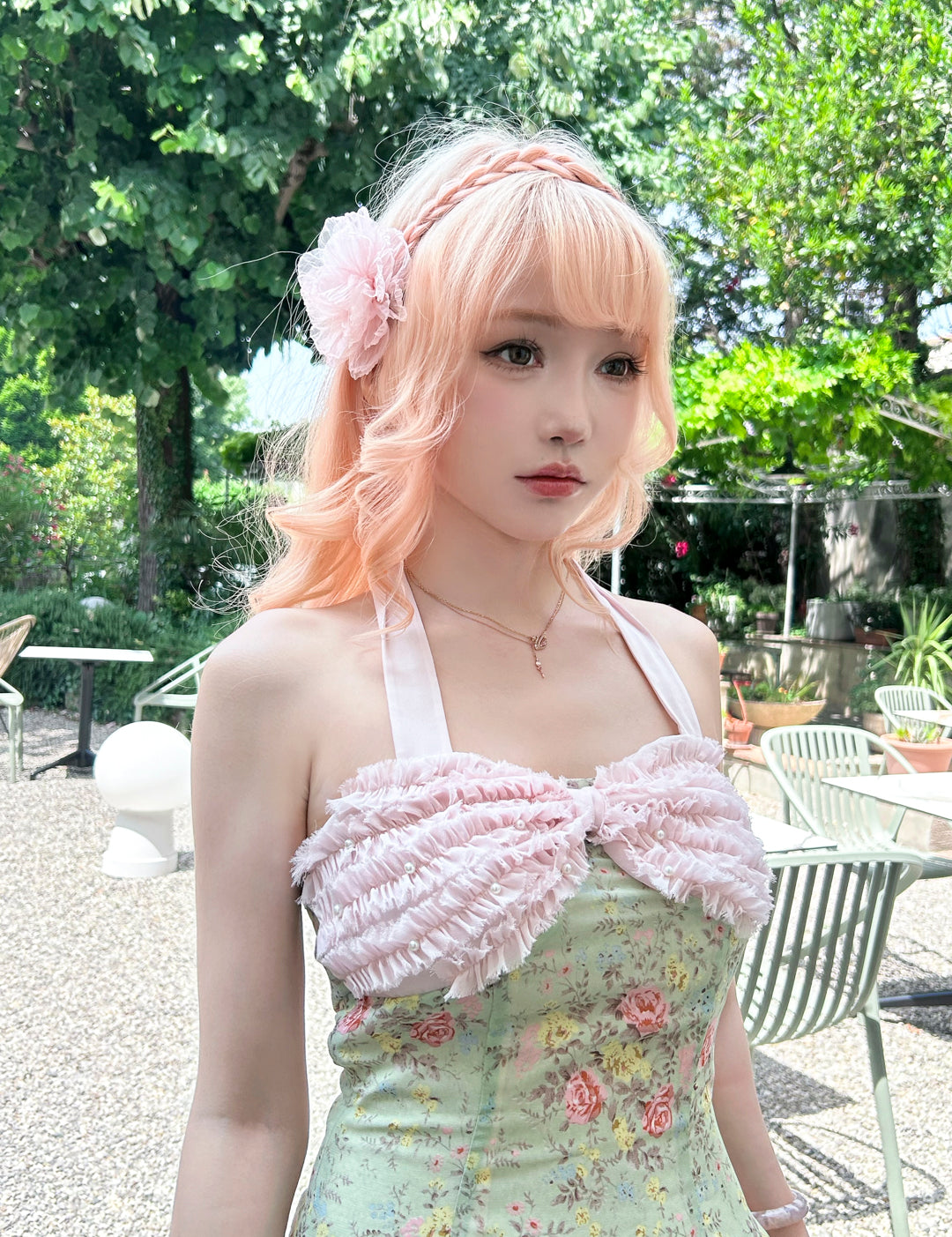 Woman with pastel pink hair and floral headband wearing a floral dress outdoors.