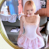 Woman in pink hair wearing a pastel pink ballet  dress with floral pattern outfit in front of a mirror.