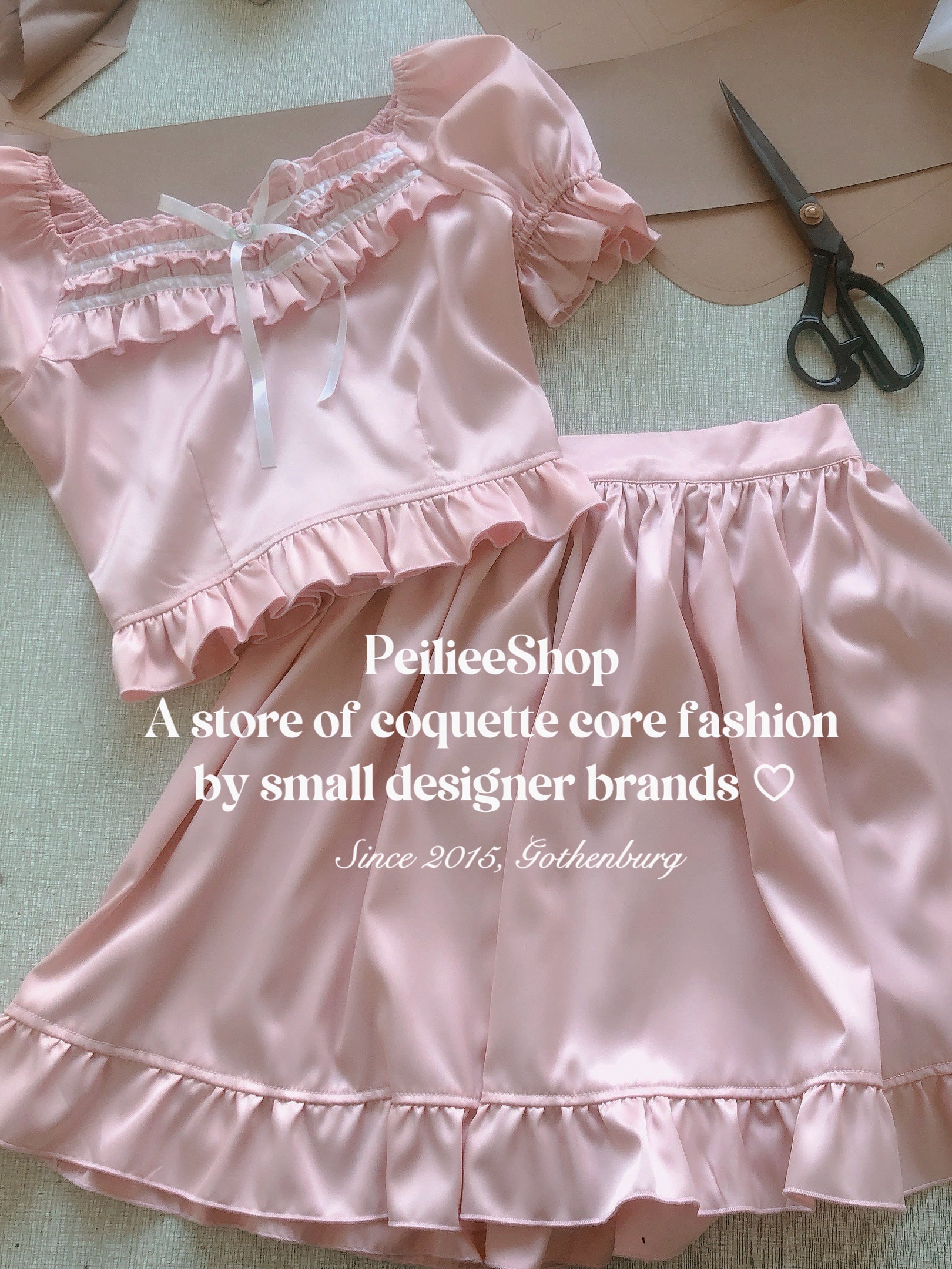 Pink outfit with ruffles on a light surface with scissors, featuring Peilieeshop branding.